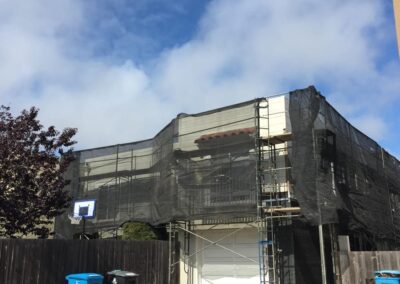 A house under construction with scaffolding and a blue trash can in front.